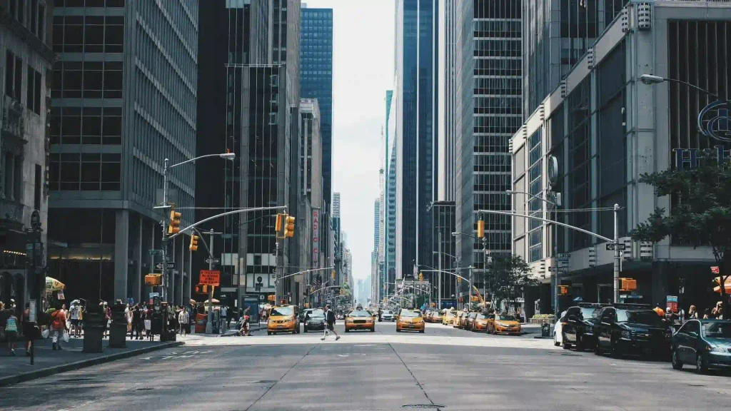 Broad city avenue in New York City flanked by towering skyscrapers, with the yellow taxis lined up along the open urban street