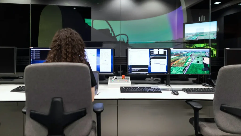 Operator sitting at a control room desk viewing multiple computer screens with software code and geographic mapping data